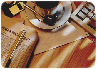 Na zdjęciu widać wiele elementów na biurku: filiżankę z kawą, klawiaturę, dyskietkę oraz dokumenty.